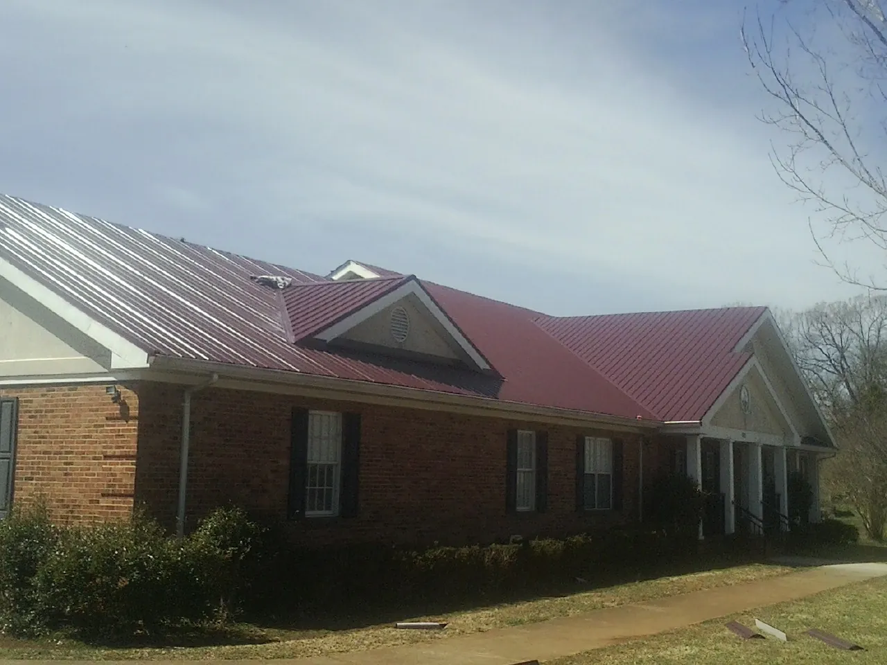 Red metal roof with gabled entries on a long brick building, from a Hail Damage Roof Repair job in Bruington