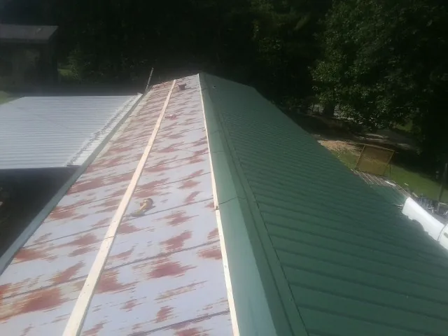 Old rusted panels beside newly installed green metal roofing — Wind Damage Roof Repair by Roofing Brothers in Bruington
