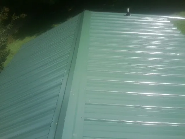 New green metal panels meeting at the ridge of a roof — Flat Roof Repair work by our crew in Bruington
