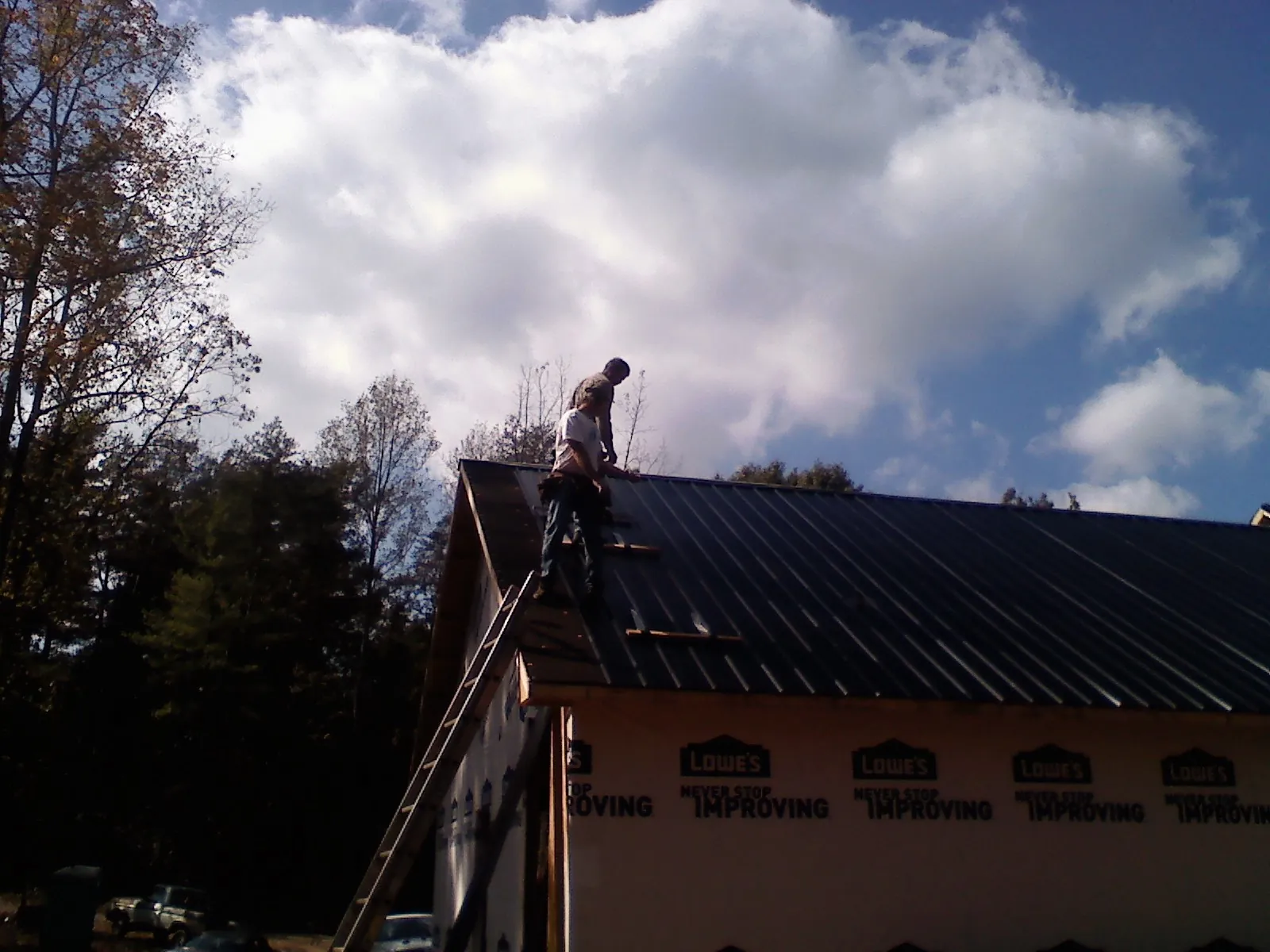 Roofer fastening dark metal panels high against a cloudy sky, from a Roof Inspection job in Bruington