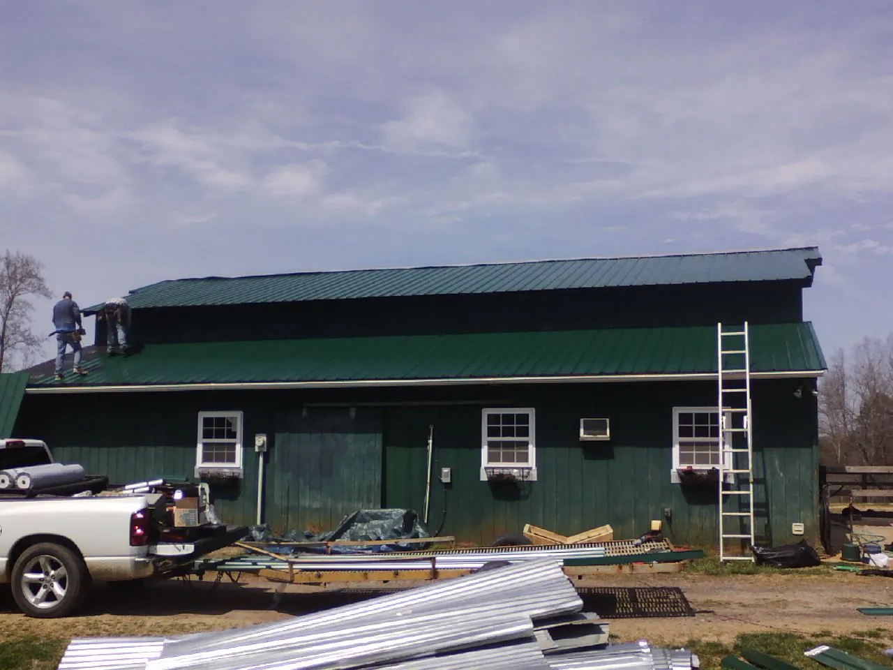 Crew installing green metal roofing on a large green barn in Bruington