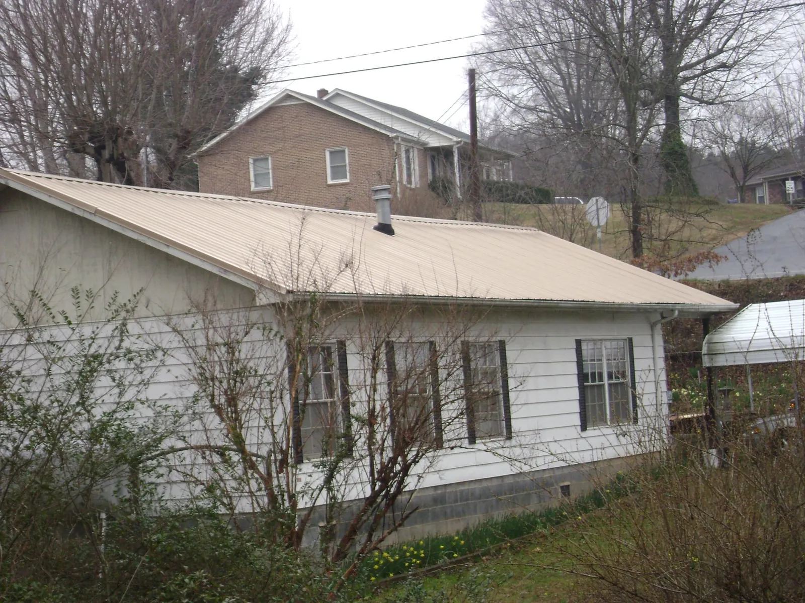 Tan metal roof on a white sided house set into a hillside — Commercial Roofing by Roofing Brothers in Bruington